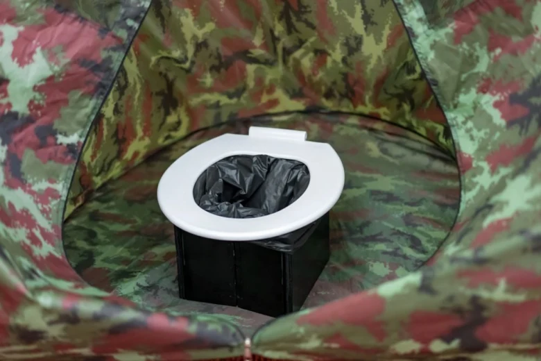 Mobilní záchod v stanu s černou taškou na odpadky.