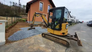 Žlutý bagr rozkládá štěrkovou vrstvu pro zámkové dlažbové schody.