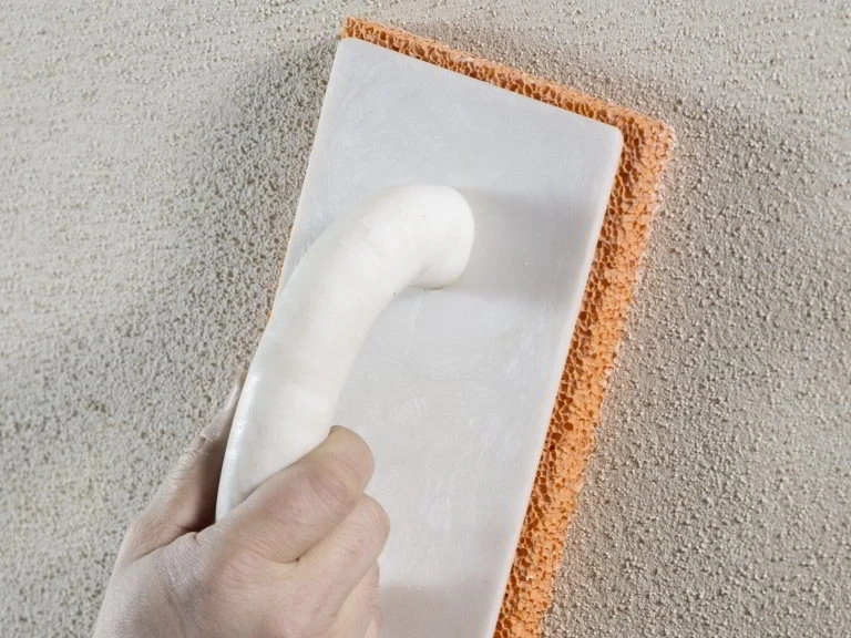 Ruka s špachtlí aplikuje materiál na nástroj pro opravu fasády.