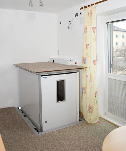 Domácí výtahová plošina s dřevěnou deskou u okna.