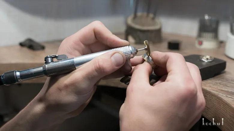 Jewelry maker uses polishing machine on silver jewelry piece.