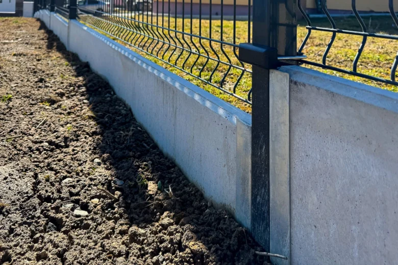 Nově instalovaný betonový základ s kovovým plotem na svahu.