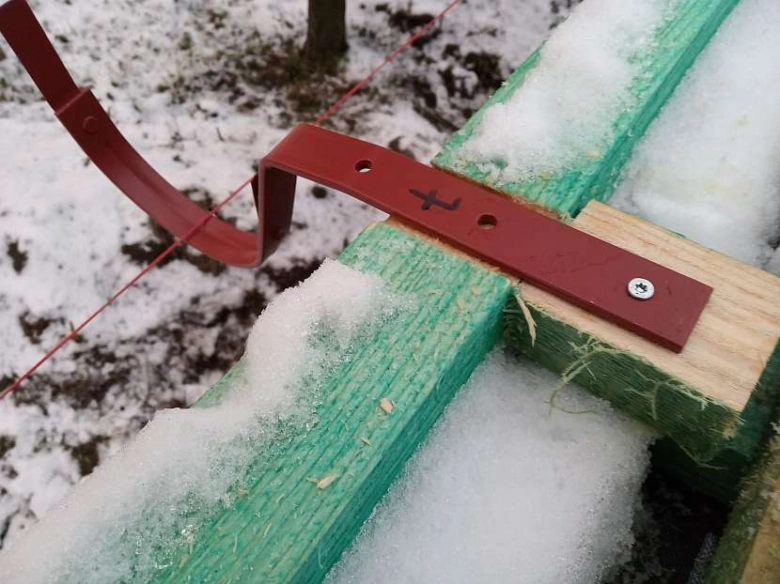 Ohnutý okapový hák na dřevěném trámu ve sněhu