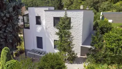 Moderní bílá fasáda rodinného domu obklopena zelenou vegetací.