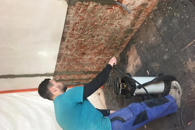 Muž nanáší sanační omítku na cihlovou zeď během rekonstrukce.