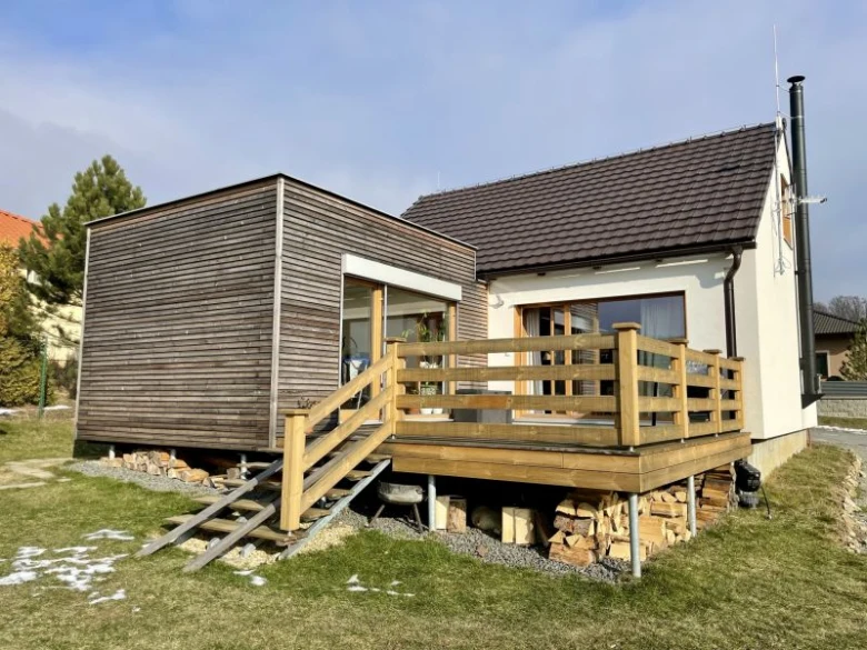 Přístavba domu s dřevěnou terasou připojená k hlavní budově.