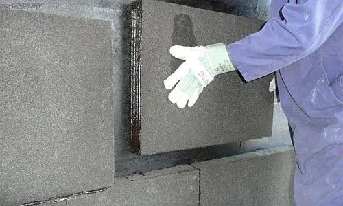 Montážní pracovník s pěnovým sklem v izolaci stavebního objektu.