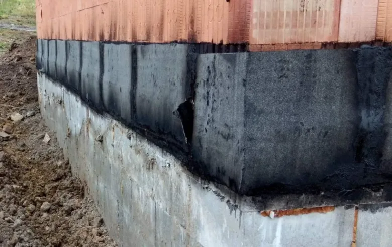 Detailní pohled na zpětný spoj hydroizolace mezi betonem a cihlovou zdí.