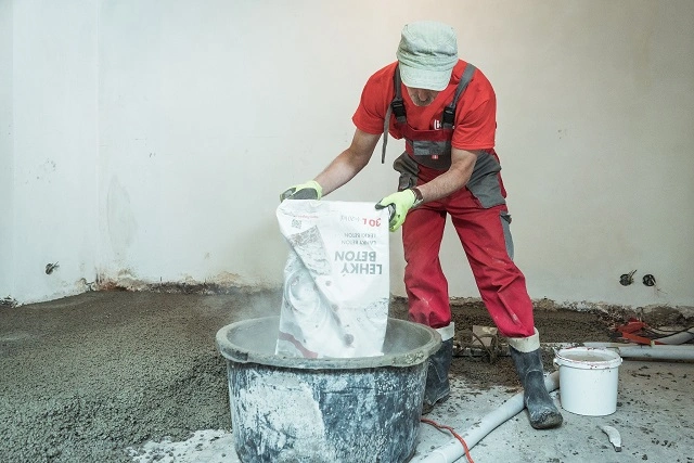 Muž nalévá lehčený beton z pytle do kbelu na staveništi.