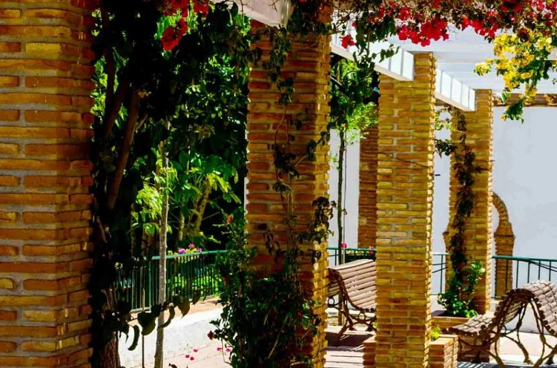 Zděná zahradní pergola s lavičkami pod pláštíkem zelené vegetace.