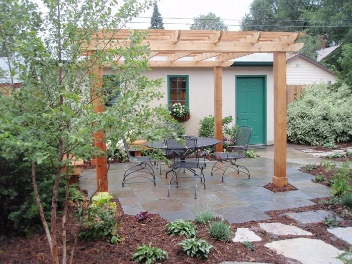 Dřevěná pergola nad zahradním posezením s nábytkem.