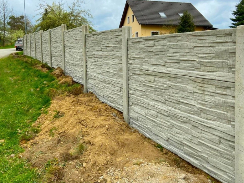 Nový betonový plot s kamennou úpravou postavený na svahu vedle silnice.