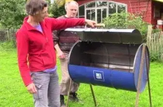 Dva lidé stojí u udírny vyrobené ze sudu na trávníku.
