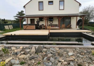 Nová dřevěná terasa na svahu u domu s vodním prvkem.
