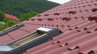 Červená tašková střecha s okny do podkroví na pozadí zelených hor.