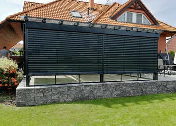 Černá roletová pergola na kamenném podkladu u domu.