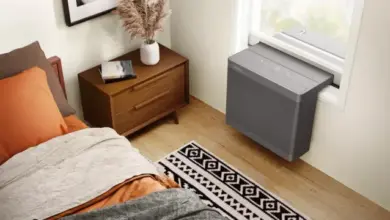 Šedý okenní čistič vzduchu v ložnici vedle nočního stolku.