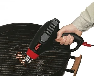 Ruční horkovzdušná pistole směřuje na uhlí v grilu pro kouření dřeva.