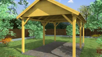Dřevěná pergola s střechou na trávníku mezi stromy.