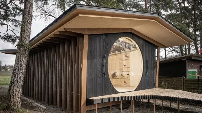 Moderní dřevěná chata s kruhovým oknem v lese.