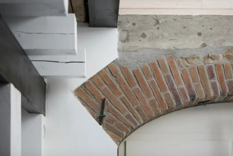 Detail staré stodoly s cihlovým obloukem a dřevěnými trámy.