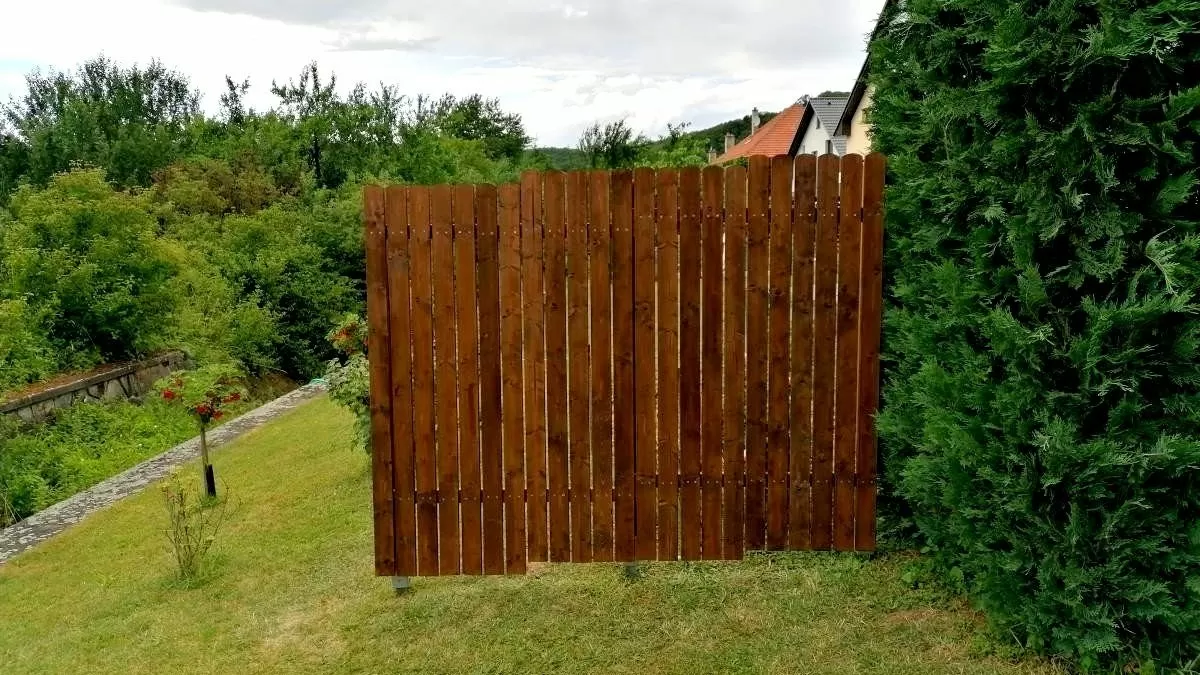 Dřevěný plot z prken na svahu s trávníkem.