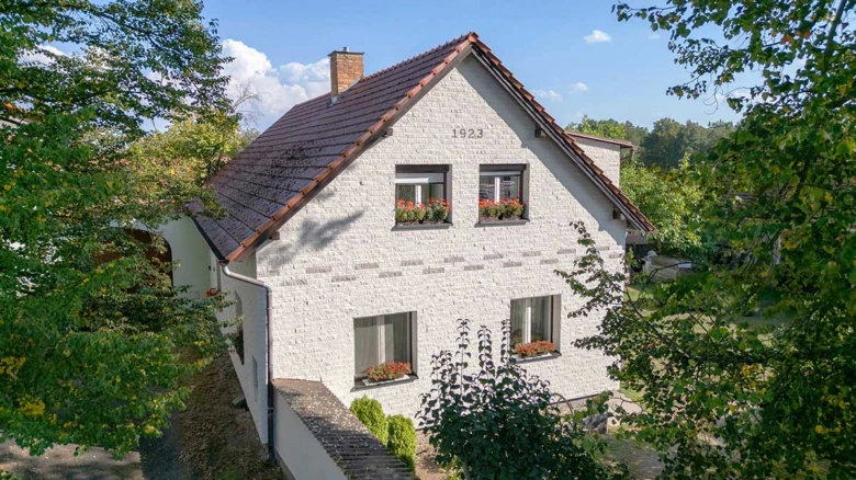 Bílá fasáda rodinného domu s květinovými boxy na oknech.