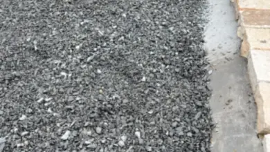 Čerstvě položená štěrková cesta s betonovými obrubami a kamenným lemem.