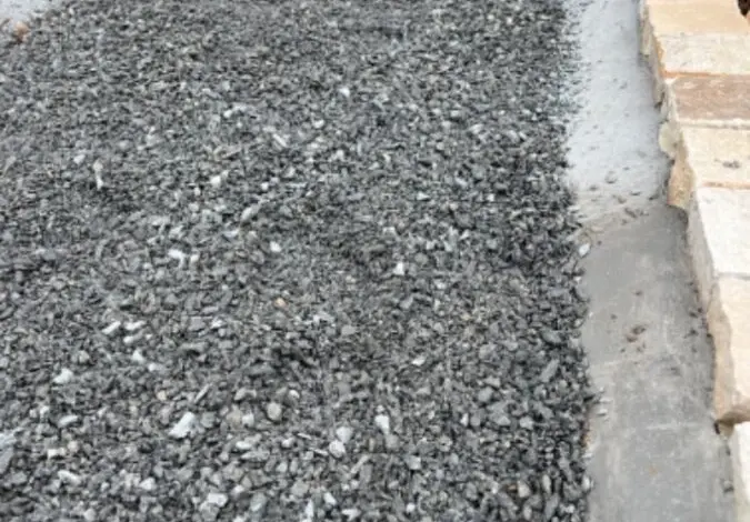 Čerstvě položená štěrková cesta s betonovými obrubami a kamenným lemem.