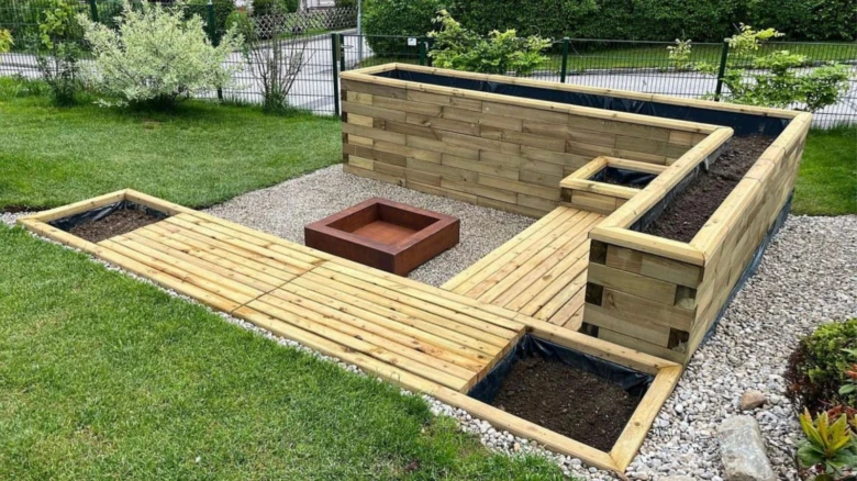 Venkovní ohniště s dřevěnými sedacími úseky a kvetinovými záhonky.