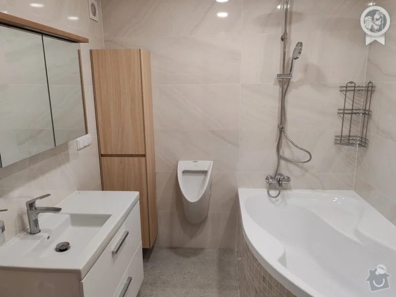 Moderní koupelna po rekonstrukci s bílými sanitami a dřevěnou skříni.