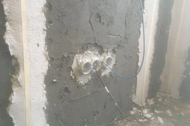Tři elektrické trubičky v zdi při nanášení sanační omítky.