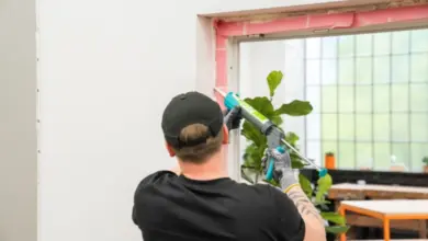Muž nanáší těsnicí hmotu na okenní rámeček při výměně oken.