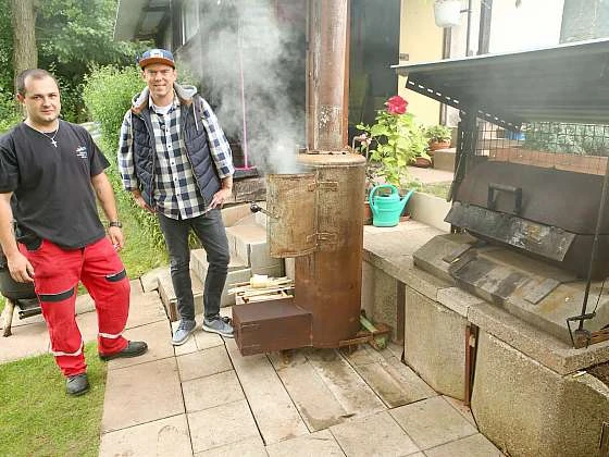 Dva muži u grilu vyrobeného z bojleru na zahradě.