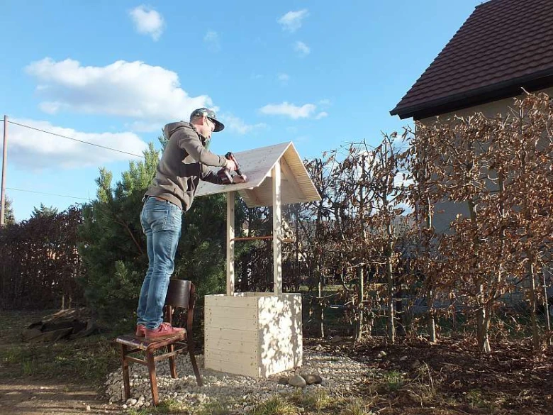 Muž staví dřevěný rumpál venku na zahradě.