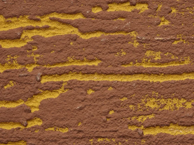 Detail světle hnědé fasády s odlupujícím se nátěrem.