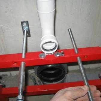 Červený nosný rám pro instalaci závěsného WC vedle odpadního potrubí.