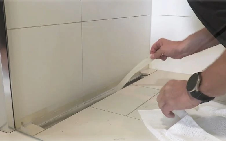 Muž nanáší sanitární silikon na spoj dlažby v koupelně.