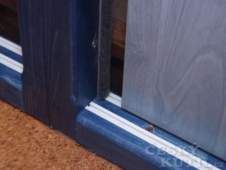 Detailní pohled na kolejnici vestavěné skříně s modrým rámem.