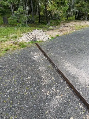 Kamenná cesta s kovovým okrajem v lese pro údržbu cest.
