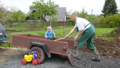 Muž tlačí vozík s dítětem na štěrkové příjezdové cestě k domu.