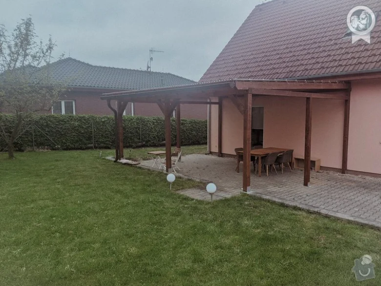 Hotová dřevěná pergola připojená k domu s venkovním nábytkem.